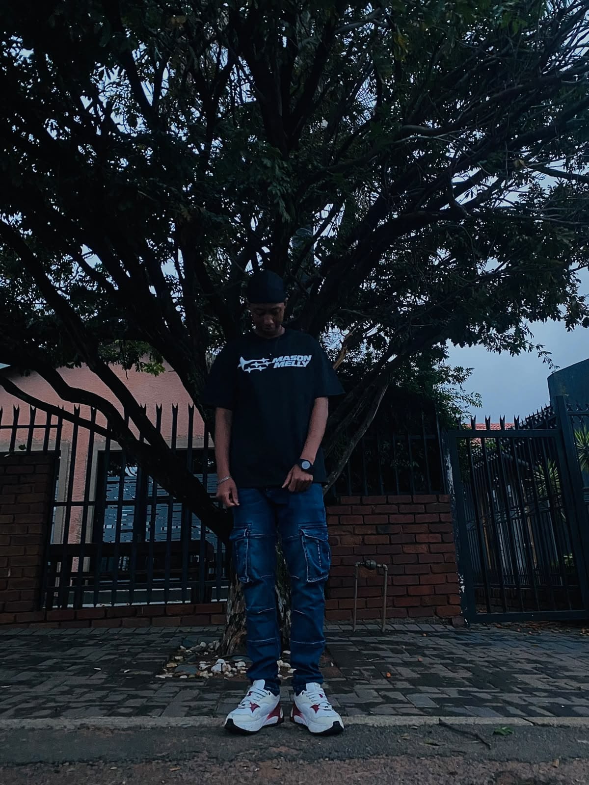Model wearing a black Mason Melly tee and blue cargo jeans under a tree